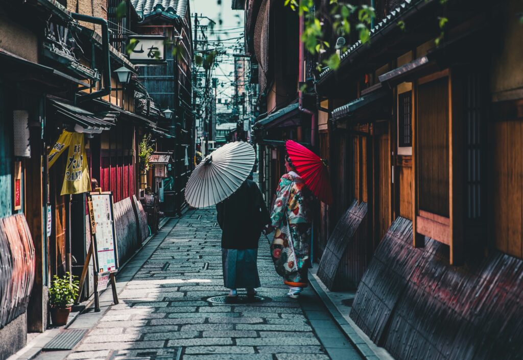 A couple in kimonos walking down a street, holding traditional Japanese umbrellas.