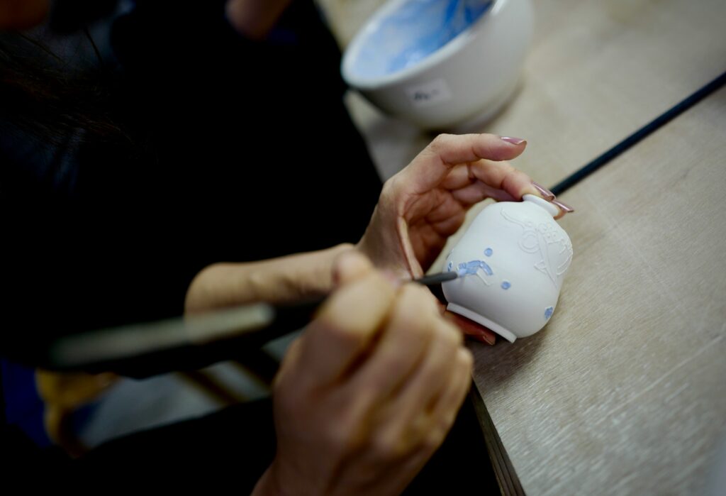 A person carefully paints designs onto a ceramic vase.