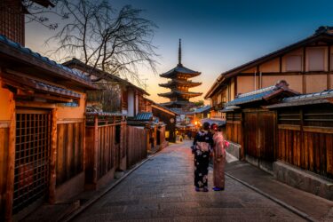 Two girls in kimonos take a selfie in front of a pagoda in Kyoto at sunset