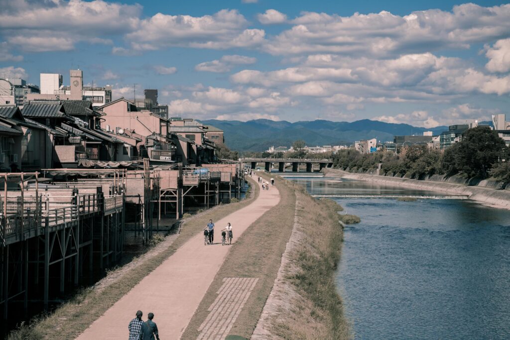 A clean and clear Kamogawa river flowing through Kyoto, Japan, with lush greenery and traditional buildings lining the banks.